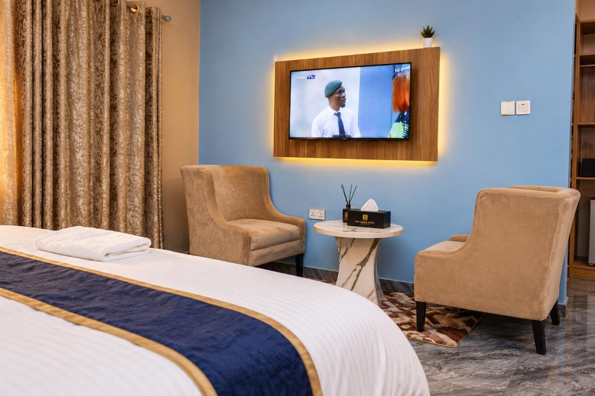 Warm, comfortable standard hotel room with a king-size bed, seating area, TV and blue accent wall at PEB Global Hotel